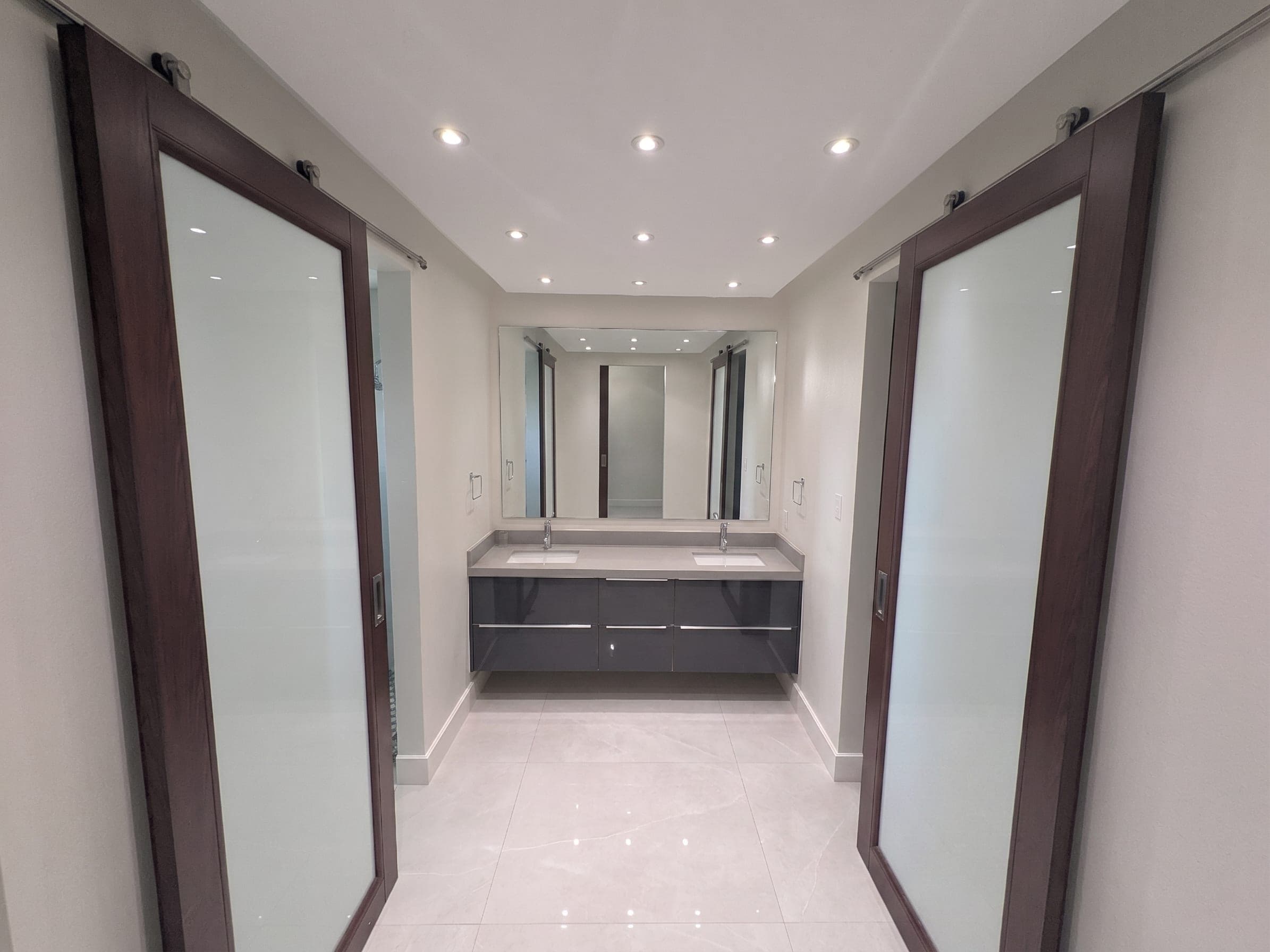 Primary bathroom vanity with double sinks framed by wood-trim sliding glass doors
