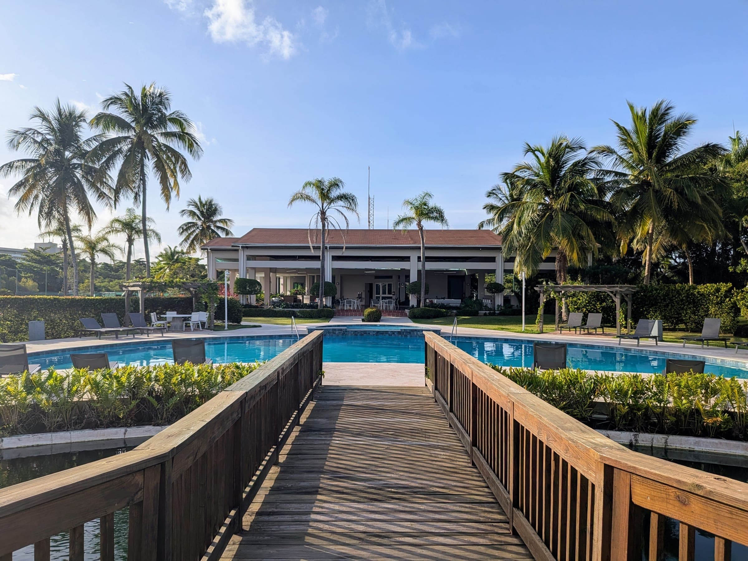 Wooden footbridge over a reflecting pool leading to the pavilion and pool deck